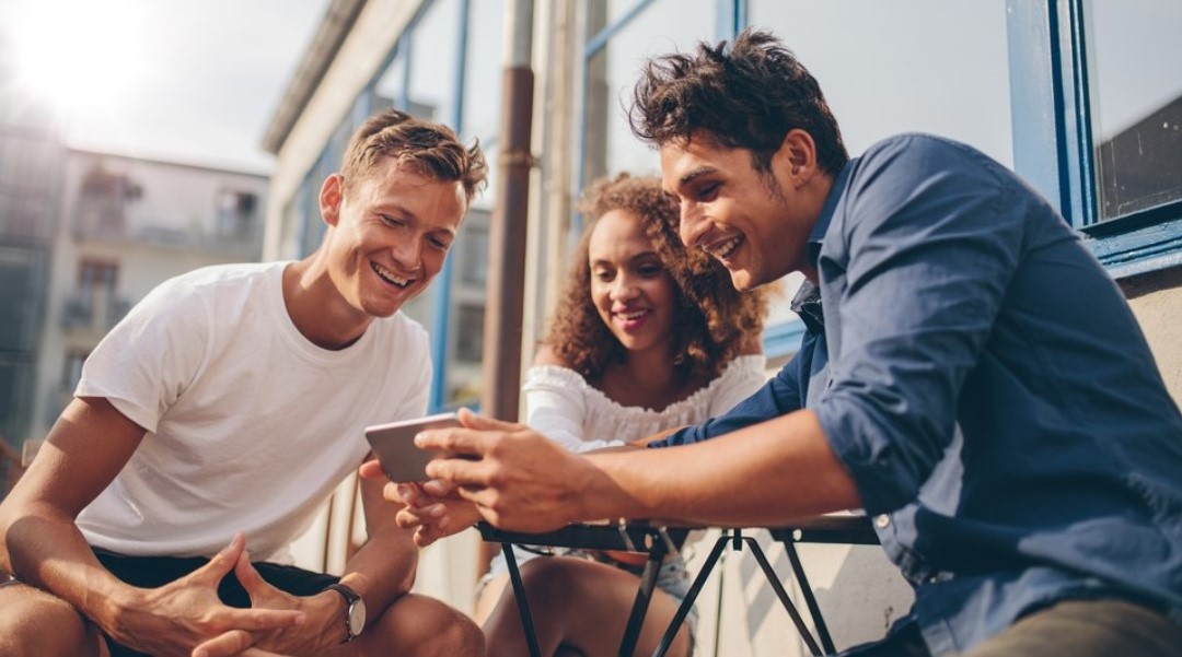 Two men and a woman are outdoors looking at a phone together